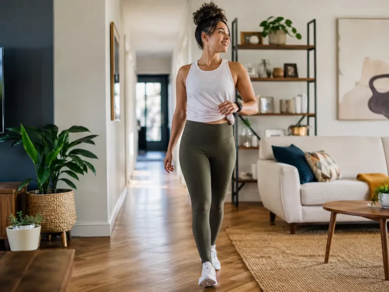 Home Een energieke vrouw wandelt door haar woonkamer en laat zien hoe je thuis makkelijk meer beweging in je dag brengt.